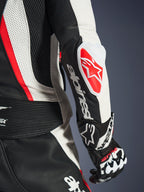 Nahaufnahme des Alpinestars Stella GP-R7 2-Teiler-Lederanzugs für Damen in Schwarz, Weiß und Rot Fluo, mit dem GP DFS RR Ellbogenschleifer, rotem Stern-Logo, weißer Alpinestars-Wortmarke auf dem Unterarm sowie detailliertem perforiertem Leder und Akkordeon-Stretch-Einsätzen.