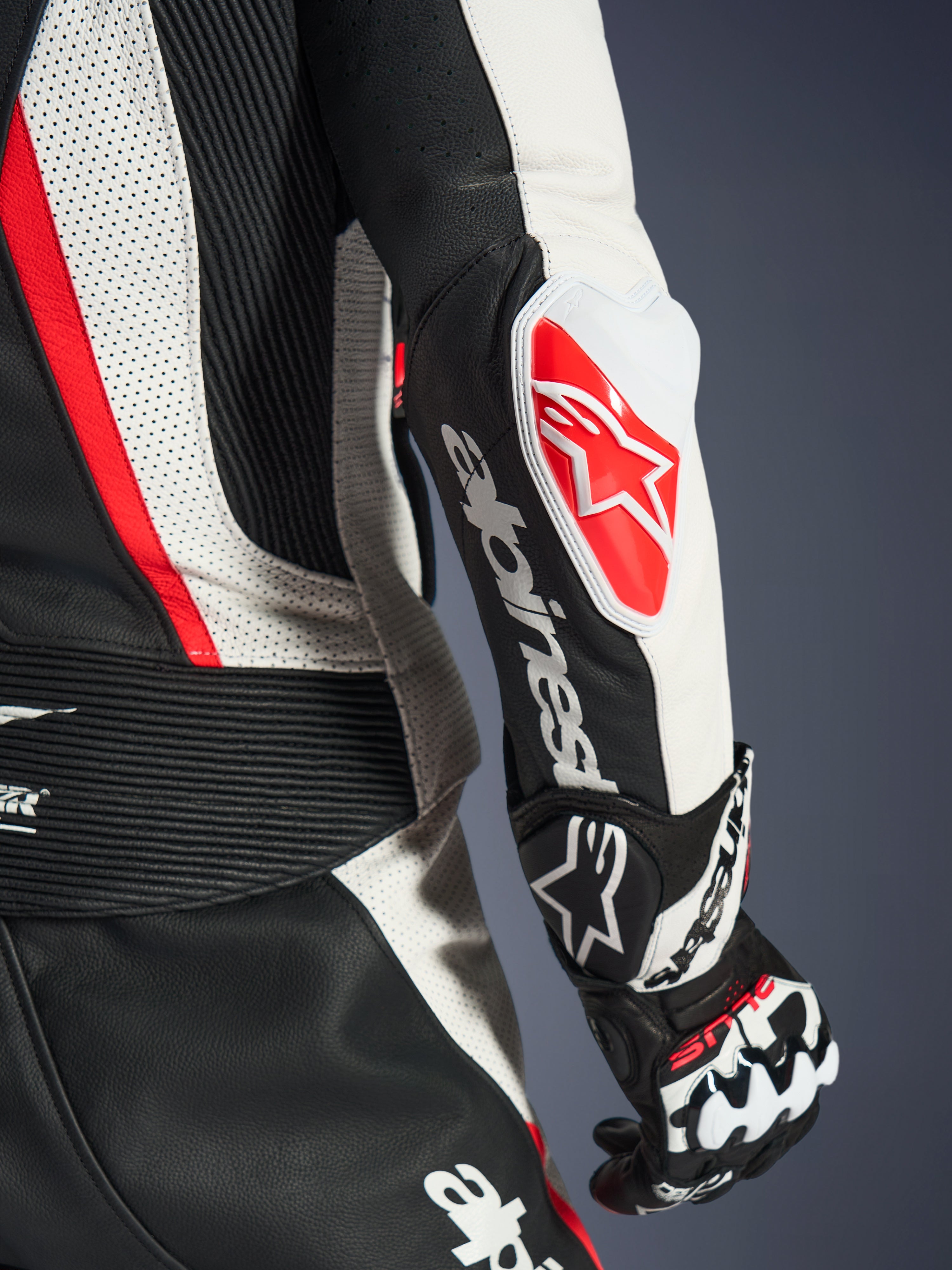 Nahaufnahme des Alpinestars Stella GP-R7 2-Teiler-Lederanzugs für Damen in Schwarz, Weiß und Rot Fluo, mit dem GP DFS RR Ellbogenschleifer, rotem Stern-Logo, weißer Alpinestars-Wortmarke auf dem Unterarm sowie detailliertem perforiertem Leder und Akkordeon-Stretch-Einsätzen.