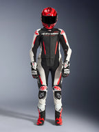 Alpinestars Stella GP-R7 2-teiliger Damen-Lederanzug in Schwarz, Weiß und Fluorot, Ganzkörperansicht einer Fahrerin mit passendem Rennhelm, Handschuhen und Stiefeln, mit perforierten Einsätzen und aerodynamischem Design für Rennstrecke und Straße.