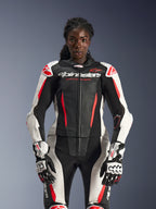 Weibliches Model im Alpinestars Stella GP-R7 2-Teiler-Lederanzug in Schwarz, Weiß und Red Fluo, mit perforierten Lederbahnen und passenden GP Pro Handschuhen, anatomisch optimiert für Fahrerinnen.
