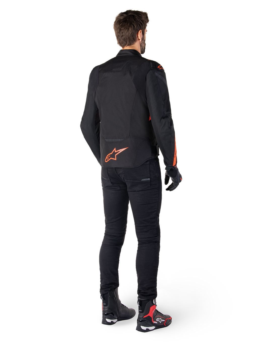 Alpinestars T-Jaws V4 Wasserdichte Jacke, Schwarz und Fluo-Rot, R&uuml;ckansicht getragen von einem m&auml;nnlichen Fahrer, mit einem leuchtend roten Fluo-Logo auf dem R&uuml;cken, kombiniert mit schwarzer Motorradhose und technischen Stiefeln, sportliche Motorradbekleidung.