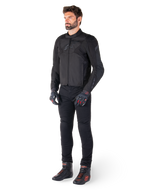 Männliches Modell in der Alpinestars T-Jaws V4 Wasserdichten Jacke in Schwarz, kombiniert mit schwarzer Motorradhose, schwarzen Handschuhen mit roten Akzenten und schwarzen Motorradschuhen, sportliche Passform, dezentes Branding, weißer Hintergrund