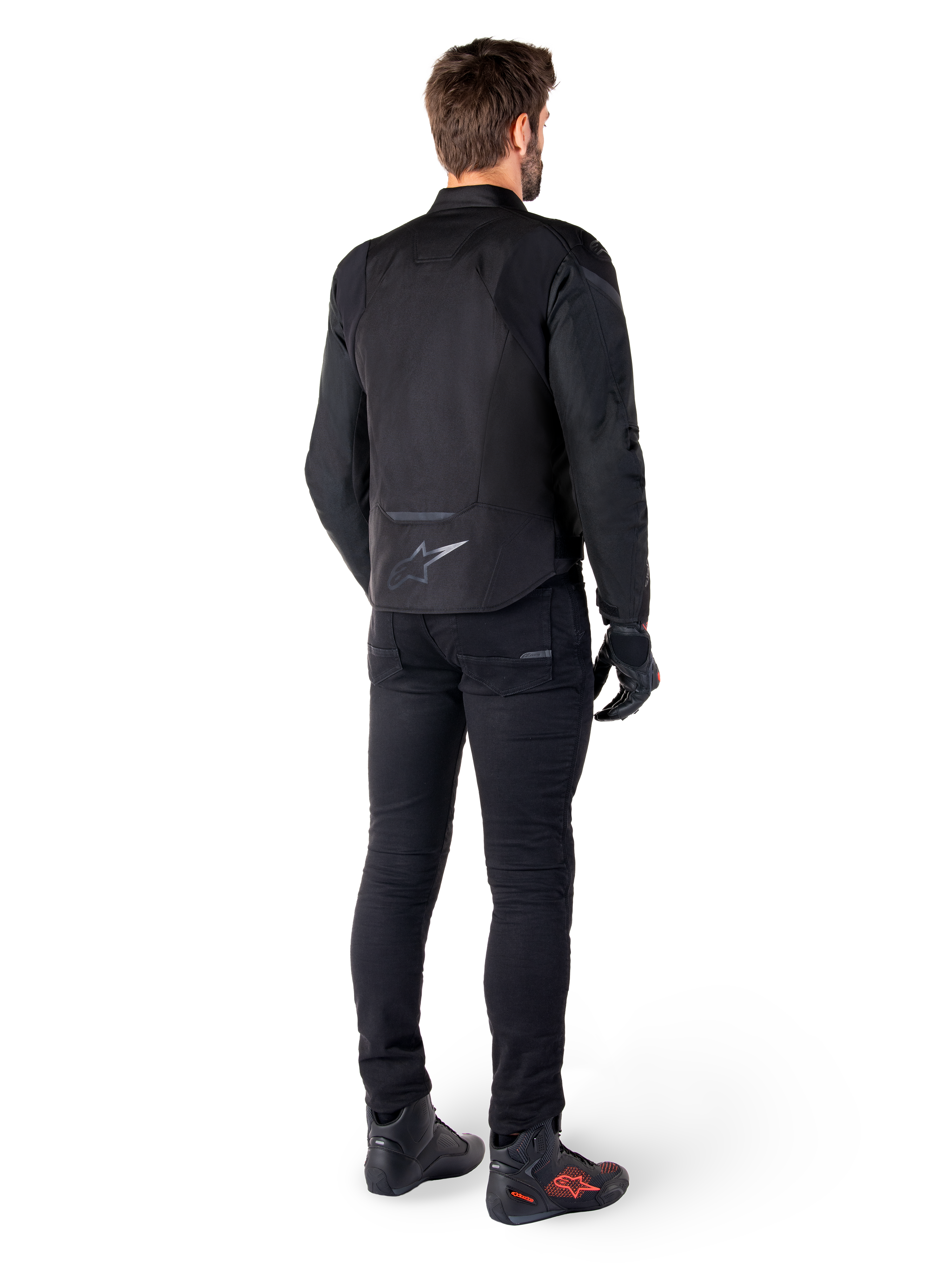 Alpinestars T-Jaws V4 Wasserdichte Jacke, Schwarz, Rückansicht am Modell mit schwarzer Motorradhose und Stiefeln, zeigt die sportliche Textilkonstruktion und das Alpinestars-Logo am unteren Rücken.