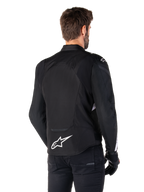 Alpinestars T-Jaws V4 Wasserdichte Jacke, Schwarz und Weiß, Rückansicht, Textil-Sportmotorradjacke mit weißem Logo am unteren Rücken, getragen mit schwarzen Handschuhen und Hosen, mit einer überarbeiteten sportlichen Silhouette