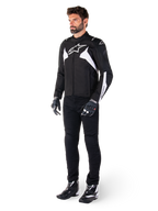 Männliches Model trägt die Alpinestars T-Jaws V4 Waterproof Jacke in Schwarz und Weiß, sportliche Textiljacke mit weißem Stern-Logo und Ärmelakzenten, kombiniert mit schwarzer Motorradhose, Handschuhen und Stiefeln für einen kompletten Road-Riding-Look.