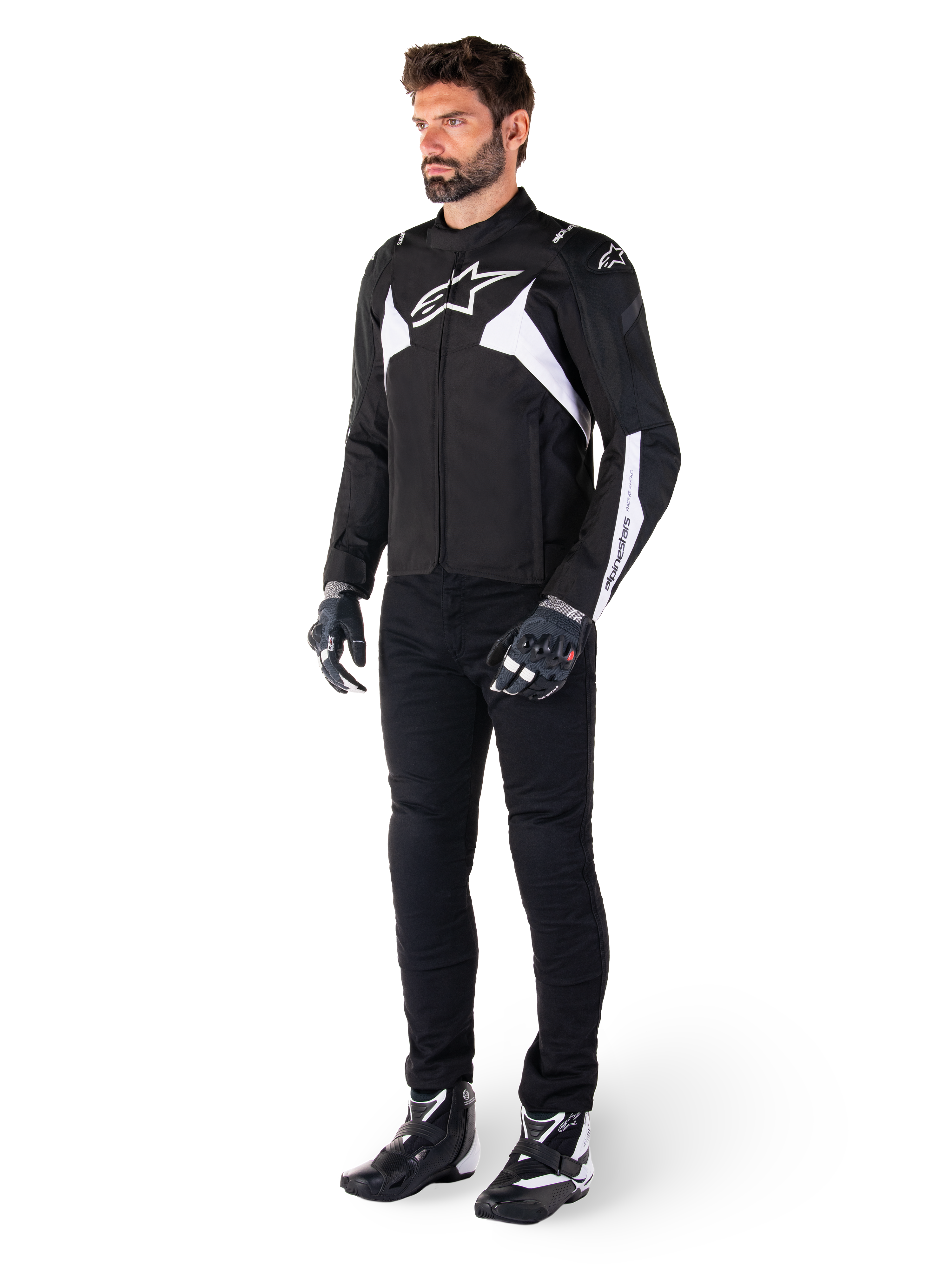 Männliches Model trägt die Alpinestars T-Jaws V4 Waterproof Jacke in Schwarz und Weiß, sportliche Textiljacke mit weißem Stern-Logo und Ärmelakzenten, kombiniert mit schwarzer Motorradhose, Handschuhen und Stiefeln für einen kompletten Road-Riding-Look.