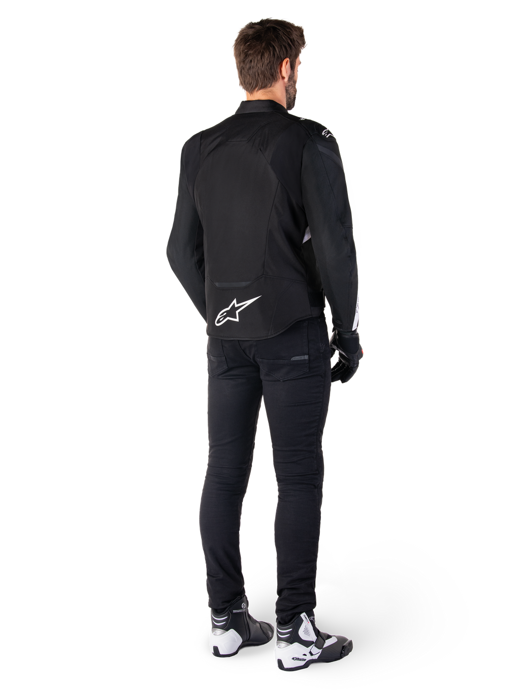 Alpinestars T-Jaws V4 Wasserdichte Jacke, Schwarz und Weiß, Rückansicht mit weißem Stern-Logo auf dem unteren Rücken, getragen von einem Model mit schwarzer Motorradhose, schwarzen Handschuhen und weiß-schwarzen Motorradstiefeln