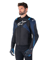 Alpinestars T-Jaws V4 Wasserdichte Jacke, Motorradjacke, Schwarz, Dunkelblau und Blithe Blue, getragen von einem Model mit passenden Handschuhen und schwarzer Hose, mit weißen Alpinestars-Logos auf der Brust und den Schultern sowie blauen Akzenten an den Ärmeln, sportliche Textil-Fahrausrüstung