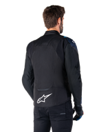 Alpinestars T-Jaws V4 Wasserdichte Jacke, Rückansicht, Schwarz mit dunkelblauen und hellblauen Details, weißes Stern-Logo am unteren Rücken, sportliche Silhouette, getragen mit schwarzer Hose und Motorradhandschuhen