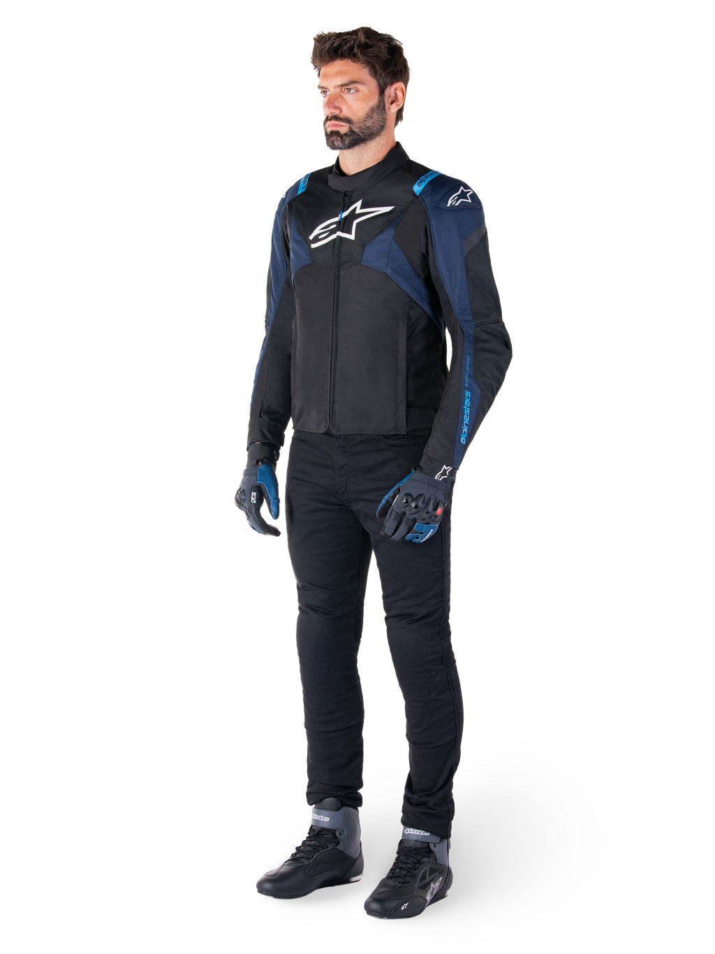 Alpinestars T-Jaws V4 Wasserdichte Jacke in Schwarz, Dunkelblau und Blithe-Blau, getragen von einem Model mit schwarzer Motorradhose und Motorradstiefeln, mit weißem Alpinestars-Logo auf der Brust und blauen Schulterakzenten, sportliche Fahrausrüstung.