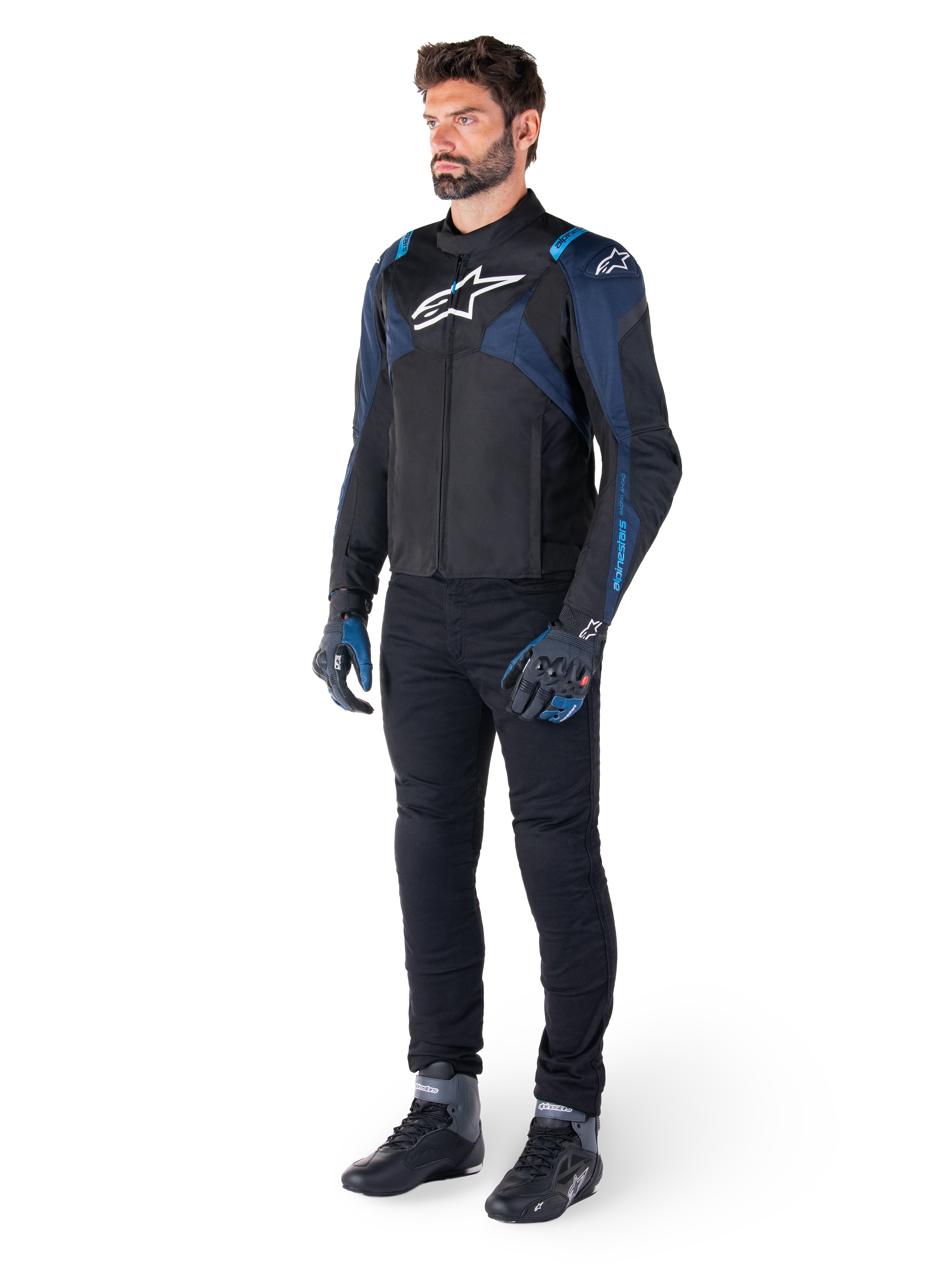 Alpinestars T-Jaws V4 Wasserdichte Jacke in Schwarz, Dunkelblau und Blithe-Blau, getragen von einem Model mit schwarzer Motorradhose und Motorradstiefeln, mit weißem Alpinestars-Logo auf der Brust und blauen Schulterakzenten, sportliche Fahrausrüstung.