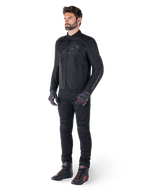 Alpinestars T-SPS V2 Waterproof Jacke, Schwarz, getragen von einem männlichen Model mit passender schwarzer Hose, schwarzen Handschuhen mit roten Akzenten und schwarzen Motorradschuhen, komplette Motorradausrüstung für Urban- und Sport-Fahrten, sauberer weißer Hintergrund