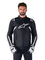 Alpinestars T-SPS V2 Waterproof Jacket in Schwarz und Weiß, Vorderansicht am Modell, wasserdichte Textil-Motorradjacke mit weißen Schulter- und Armstreifen, großes weißes Alpinestars-Logo auf der Brust, getragen mit Motorrad-Schutzhandschuhen, schlanke sportlich inspirierte Silhouette.