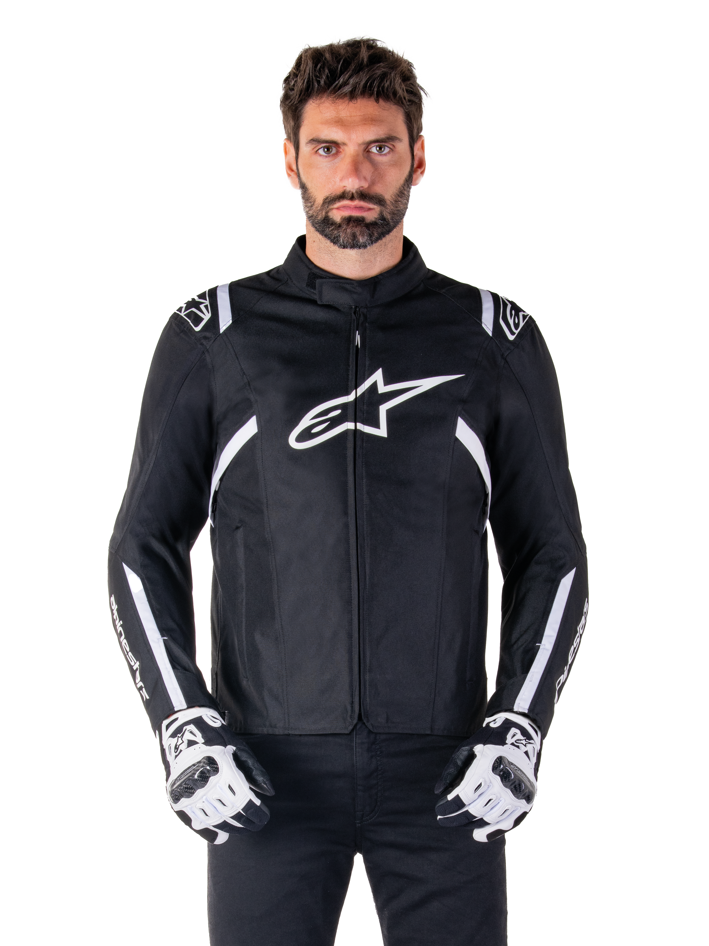 Alpinestars T-SPS V2 Waterproof Jacket in Schwarz und Weiß, Vorderansicht am Modell, wasserdichte Textil-Motorradjacke mit weißen Schulter- und Armstreifen, großes weißes Alpinestars-Logo auf der Brust, getragen mit Motorrad-Schutzhandschuhen, schlanke sportlich inspirierte Silhouette.