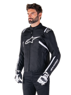 Alpinestars T-SPS V2 Waterproof Jacke, Schwarz und Weiß, getragen von einem männlichen Model mit passenden Motorradhandschuhen, Textiljacke im Sportschnitt mit weißen Alpinestars-Logos auf Brust und Schultern, „alpinestars T-SPS“-Branding am Ärmel, elegante vom Rennsport inspirierte Motorradausrüstung