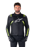 Alpinestars T-SPS V2 Waterproof Jacke, Motorradjacke, Schwarz mit weißen und neongelben Akzenten, getragen von einem Model mit schwarzen Handschuhen, mit weißem Stern-Logo auf der Brust und neongelben Streifen an Ärmeln und Schultern, sportliche Textilausrüstung für jedes Wetter