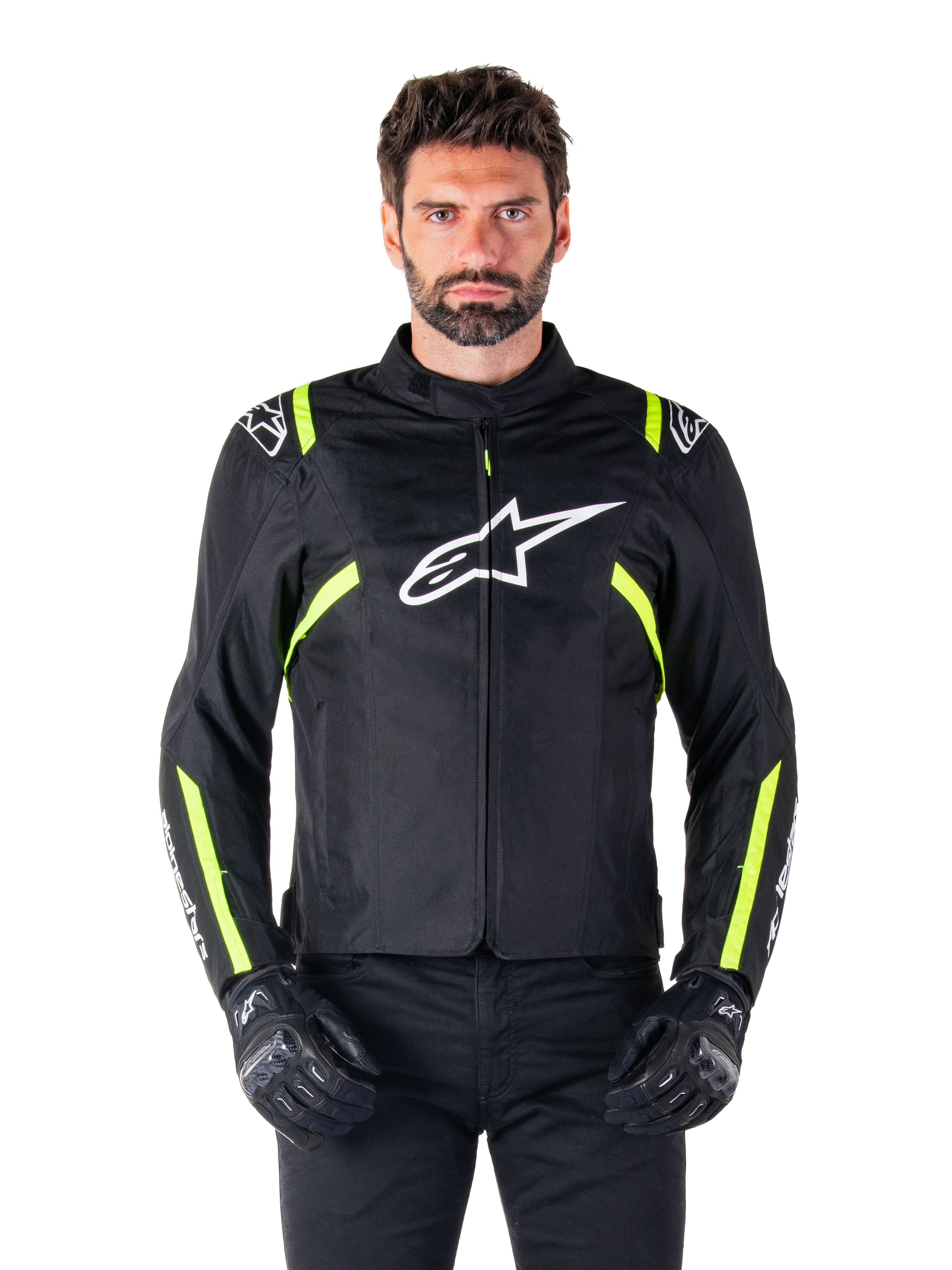 Alpinestars T-SPS V2 Waterproof Jacke, Motorradjacke, Schwarz mit weißen und neongelben Akzenten, getragen von einem Model mit schwarzen Handschuhen, mit weißem Stern-Logo auf der Brust und neongelben Streifen an Ärmeln und Schultern, sportliche Textilausrüstung für jedes Wetter
