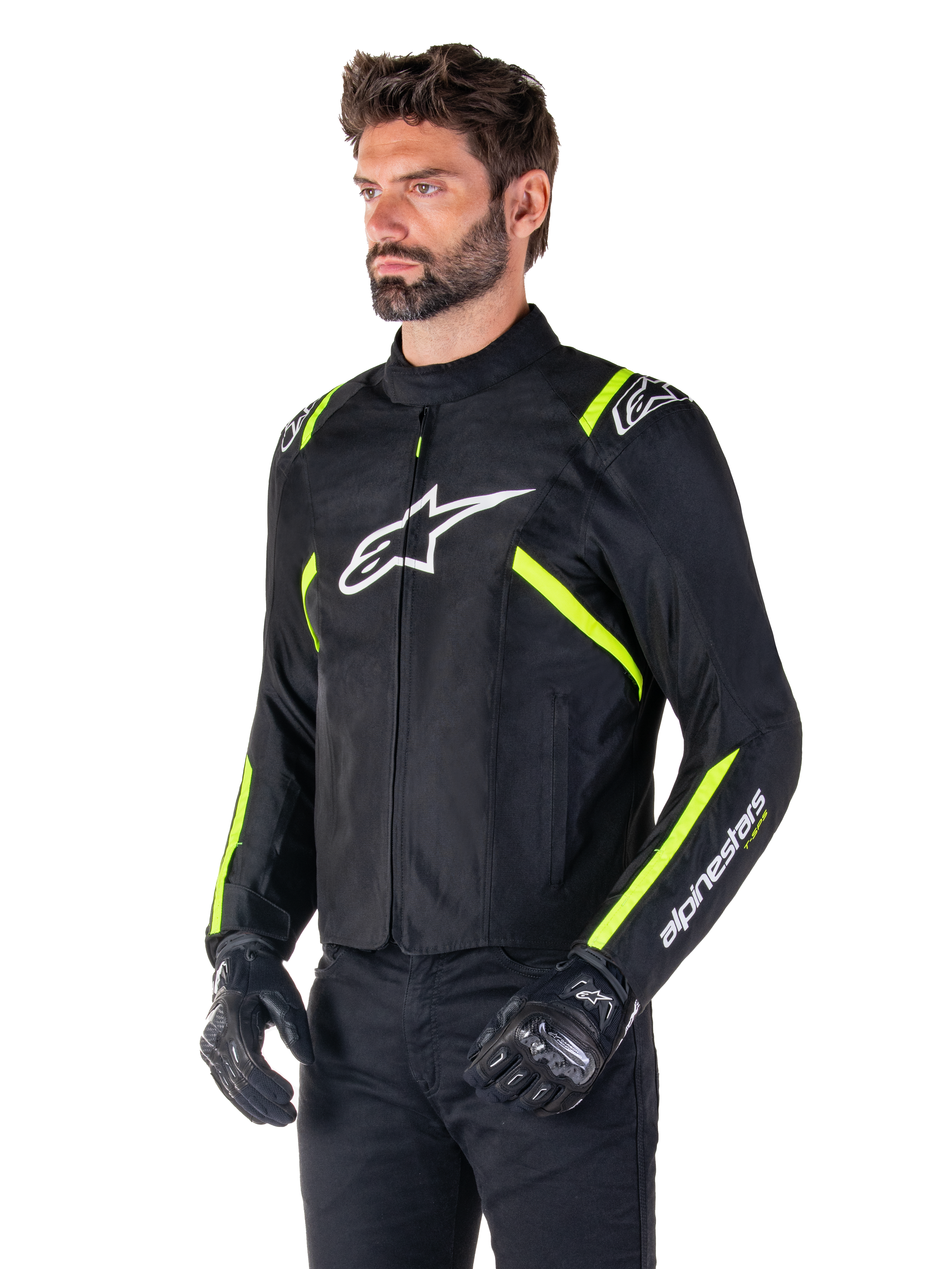 Männliches Model in der Alpinestars T-SPS V2 Waterproof Jacke, Schwarz mit weißen und gelben Fluo-Akzenten, mit einem weißen Astars-Logo auf der Brust und fluoreszierenden gelben Streifen an den Schultern und Ärmeln, kombiniert mit einer schwarzen Hose und Motorradhandschuhen, sportlich geschnittene Textil-Motorradjacke.