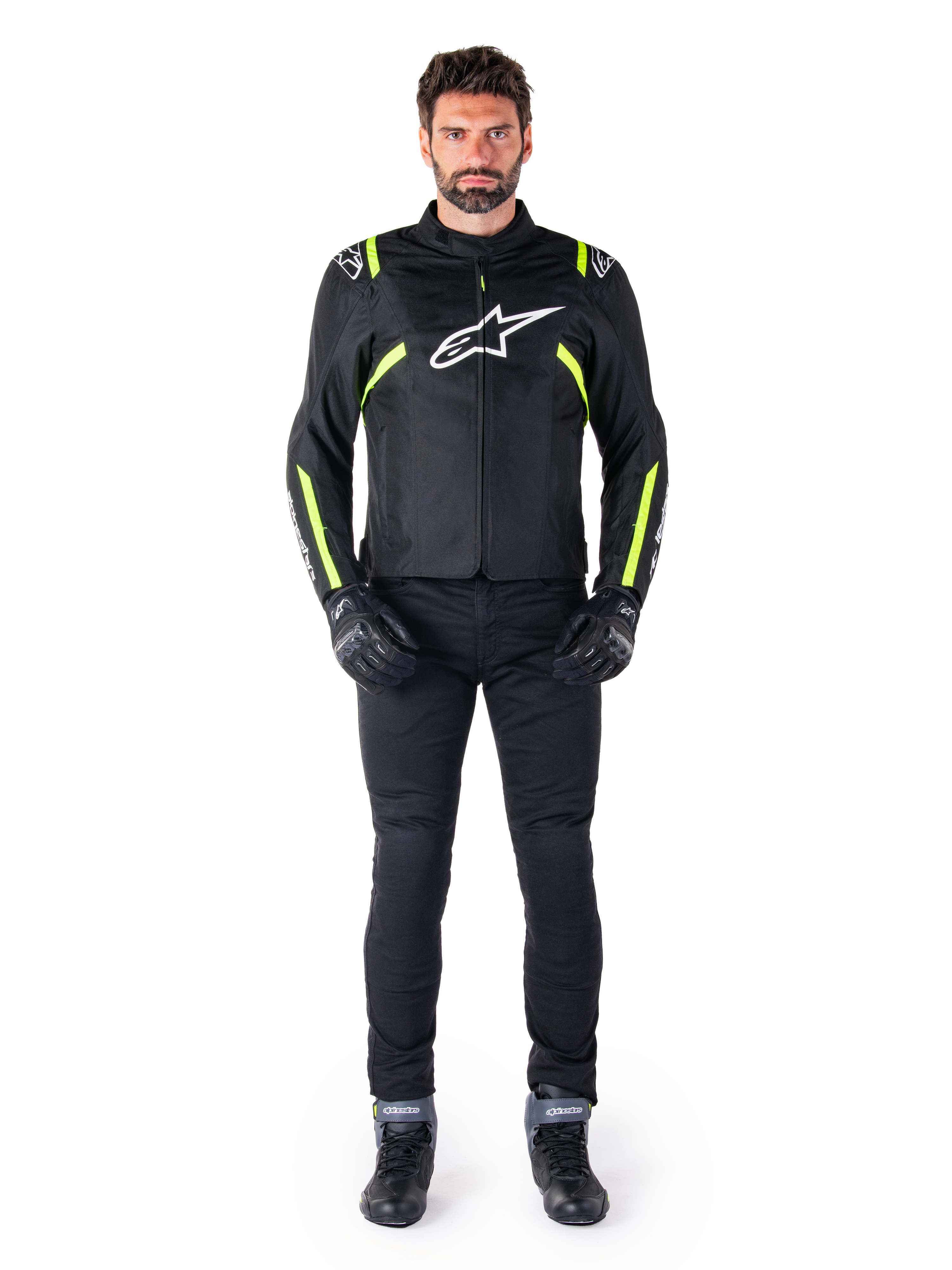 Alpinestars T-SPS V2 Waterproof Jacke, Schwarz, Weiß und Gelb Fluo, getragen von einem Model mit schwarzer Motorradhose und Handschuhen, mit weißem Alpinestars-Logo auf der Brust und fluoreszierenden Akzenten an Schultern und Ärmeln, sportlich geschnittene Motorradbekleidung