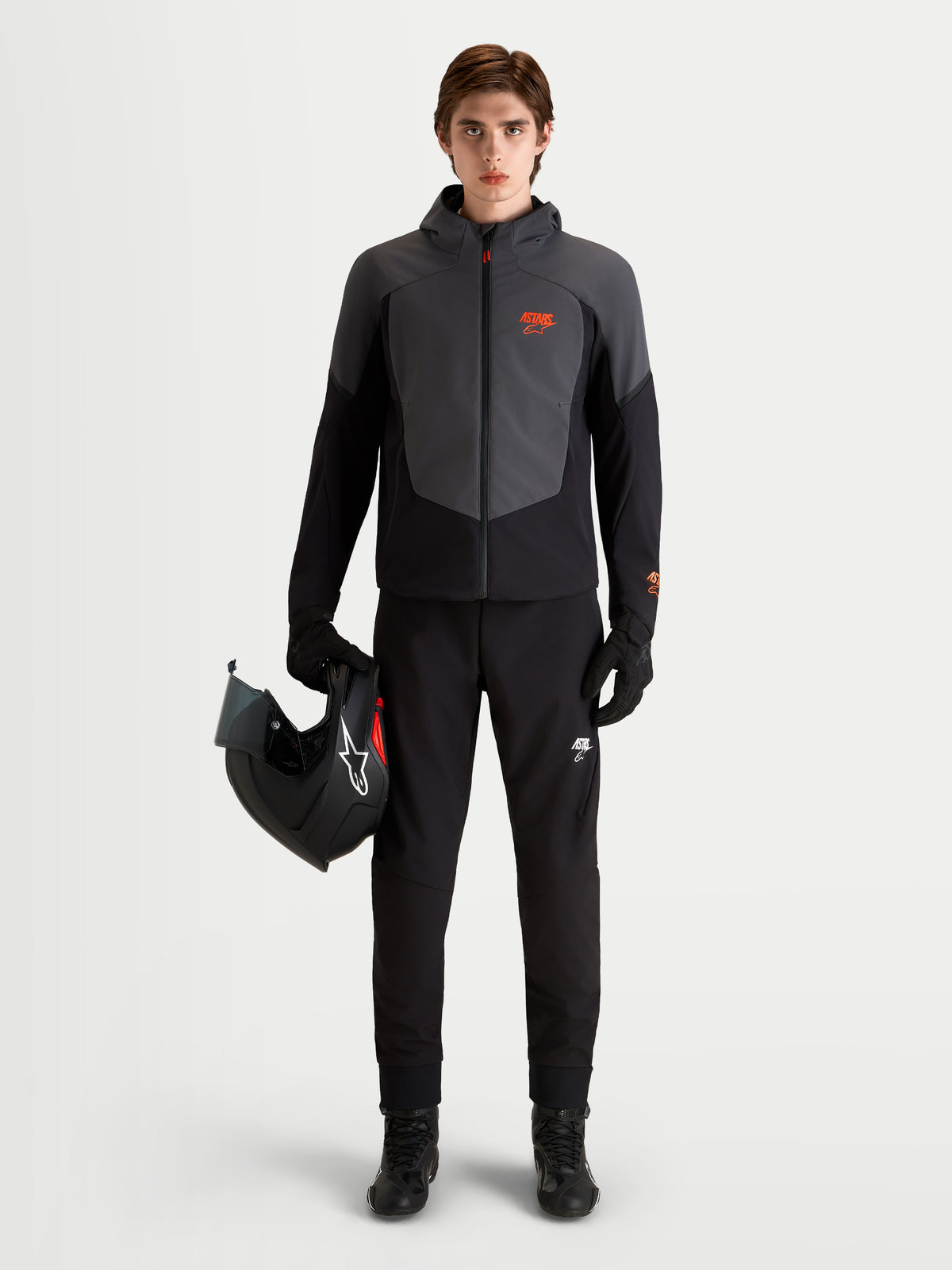 Alpinestars Aeroshell Waterproof Jacket, Men's Motorcycle Riding Jacket in Black and Dark Gray, featuring an open-slot hood and CE-certified protection, worn by a model holding a motorcycle helmet