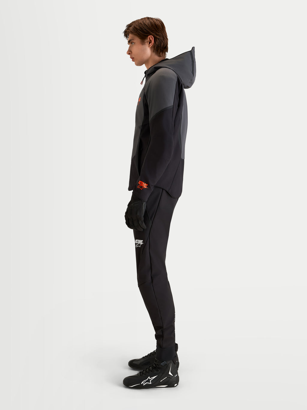 Alpinestars Aeroshell Waterproof Jacket, Men's Motorcycle Softshell Hoodie in Black and Dark Gray, featuring an open-slot hood and CE certification, worn by a model in profile view