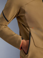 Nahaufnahme der Alpinestars Aeroshell Waterproof Jacke, Dunkelkhaki mit schwarzen und fluoreszierend orangen Akzenten, Detail der versteckten Reißverschlusstasche und des Ärmelbündchens, elastisches Softshell-Gewebe für das Motorradfahren