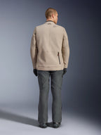 Alpinestars Borrego Drystar® Jacke, Rückansicht eines männlichen Models in der Textil-Motorradjacke in Warm Gray, kombiniert mit dunkelgrauer technischer Hose, schwarzen Handschuhen und Stiefeln, mit robustem gewachstem Canvas-Design und hinteren Dehnungszonen.