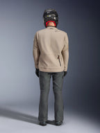 Alpinestars Borrego Drystar® Jacke, Adventure-Motorradjacke in Warm Gray, Rückansicht mit gewachstem Canvas-Look, Dehnungseinsätzen an den Schultern und einer Reißverschlusstasche am unteren Rücken, getragen mit dunkelgrauer Motorradhose und schwarzem Helm.