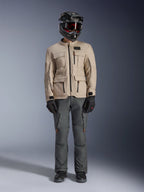 Alpinestars Borrego Drystar® Jacke in Warm Gray, Adventure-Motorradjacke mit vier Cargo-Taschen auf der Vorderseite, kombiniert mit dunkelgrauer Fahrhose, schwarzem Offroad-Helm und schwarzen Handschuhen, im robusten gewachsten Canvas-Look