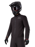 Fahrer trägt den Alpinestars AMT-8 Stretch Drystar® XF Liner, schwarze wind- und wasserdichte Stretchjacke, mit AMT-Logo auf der Brust und Drystar-XF-Branding auf dem Ärmel, kombiniert mit einem schwarzen Adventure-Helm und Schutzhandschuhen.