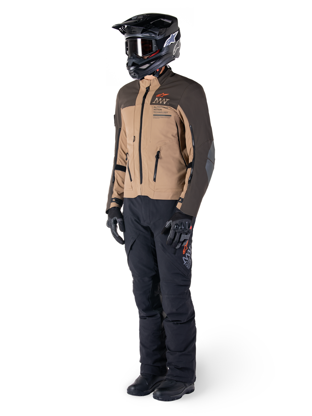Adventure-Fahrer in kompletter Ausrüstung, Alpinestars AMT-8 Stretch Drystar® XF Jacke in Dunkelbraun und Dunkelkhaki, kombiniert mit schwarzer Adventure-Hose, schwarzem Helm, Handschuhen und Stiefeln, mit orangefarbenem AMT-Branding und technischen Belüftungsreißverschlüssen für Langstreckentouren