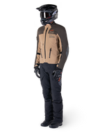 Adventure-Fahrer in kompletter Ausrüstung, Alpinestars AMT-8 Stretch Drystar® XF Jacke in Dunkelbraun und Dunkelkhaki, kombiniert mit schwarzer Adventure-Hose, schwarzem Helm, Handschuhen und Stiefeln, mit orangefarbenem AMT-Branding und technischen Belüftungsreißverschlüssen für Langstreckentouren