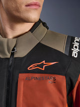 Alpinestars Andes V4 Drystar® Jacket in Walnut Rust Black, close-up of upper chest and shoulder, featuring orange A-star logo on black panel and Alpinestars branding on rust-colored section, adventure motorcycle gear detail