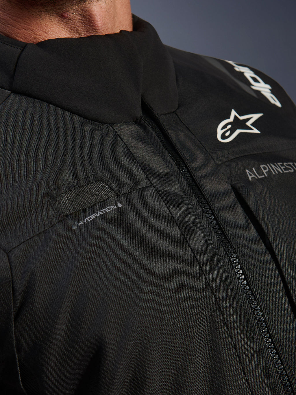 Alpinestars Andes V4 Drystar® Jacke, Schwarz, Nahaufnahme der Brustpartie mit Trinkschlauch-Schlaufe, wasserdichtem VISLON®-Frontreißverschluss und Alpinestars-Logo auf strapazierfähigem Textilmaterial