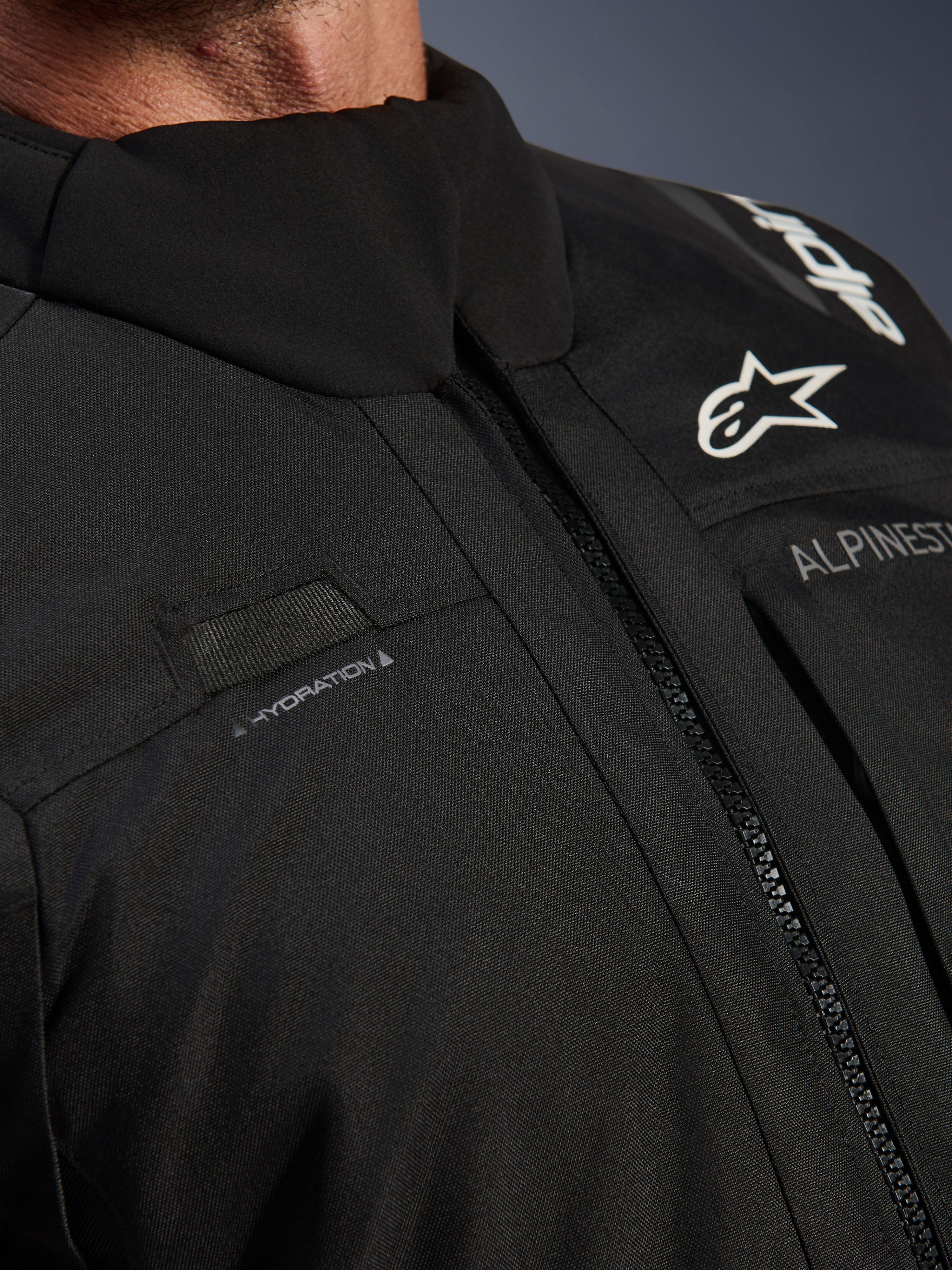 Alpinestars Andes V4 Drystar® Jacke, Schwarz, Nahaufnahme der Brustpartie mit Trinkschlauch-Schlaufe, wasserdichtem VISLON®-Frontreißverschluss und Alpinestars-Logo auf strapazierfähigem Textilmaterial