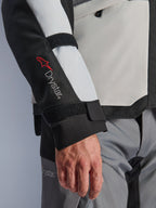 Alpinestars Andes V4 Drystar® Jacke, Adventure-Motorradjacke, eisgraue und schwarze Paneele, Nahaufnahme des Ärmels mit rotem Drystar®-Logo und verstellbaren Riemen, funktionales Textildesign für Fahrten bei jedem Wetter