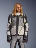 Alpinestars Andes V4 Drystar Jacke, Adventure-Touring-Motorradjacke, Dunkelgrau und Eisgrau mit neongelben Akzenten, getragen von einem Model mit passender Hose und Handschuhen, Multi-Pocket-Textildesign für Fahrten bei jedem Wetter