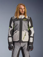 Alpinestars Andes V4 Drystar Jacke, Adventure-Touring-Motorradjacke, Dunkelgrau und Eisgrau mit neongelben Akzenten, getragen von einem Model mit passender Hose und Handschuhen, Multi-Pocket-Textildesign für Fahrten bei jedem Wetter