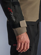 Nahaufnahme der Alpinestars Andes V4 Drystar® Jacke in Walnut und Schwarz, mit dem roten Drystar®-Logo am Unterarm und einem verstellbaren Ärmelverschluss, Teil eines technischen Adventure-Motorrad-Outfits.