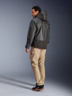 Alpinestars Mospher Waterproof Jacke in Schwarz, Rück- und Seitenprofilansicht, kombiniert mit beigefarbener Cargohose und schwarzen Sneakern, Parka-Design mit Kapuze aus Ripstop-Gewebe, Alpinestars-Branding am Ärmel, moderner urbaner Motorrad-Stil