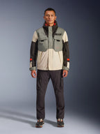 Alpinestars Mospher Waterproof Jacket in Fur Gray Black Ice, tactical-style motorcycle parka worn by a male model with dark cargo pants, multi-pocket design with color-blocked gray, cream, and black panels, urban commuter riding gear