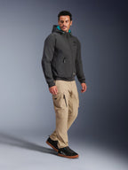 Männliches Model trägt die Alpinestars Moblast Waterproof Jacke in Schwarz, urbaner Motorrad-Hoodie mit türkis gefütterter Kapuze, kombiniert mit khakifarbener Cargohose und schwarzen Sneakern, modernes minimalistisches Design mit technischem Stretchgewebe für das Pendeln bei jedem Wetter