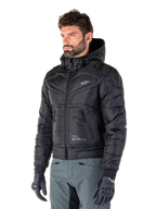 Alpinestars Mohobbs Waterproof Jacket, Black, quilted padded bomber design with a hood, worn by a man with grey riding pants and black gloves, urban streetwear-inspired motorcycle apparel featuring a small white logo on the chest.