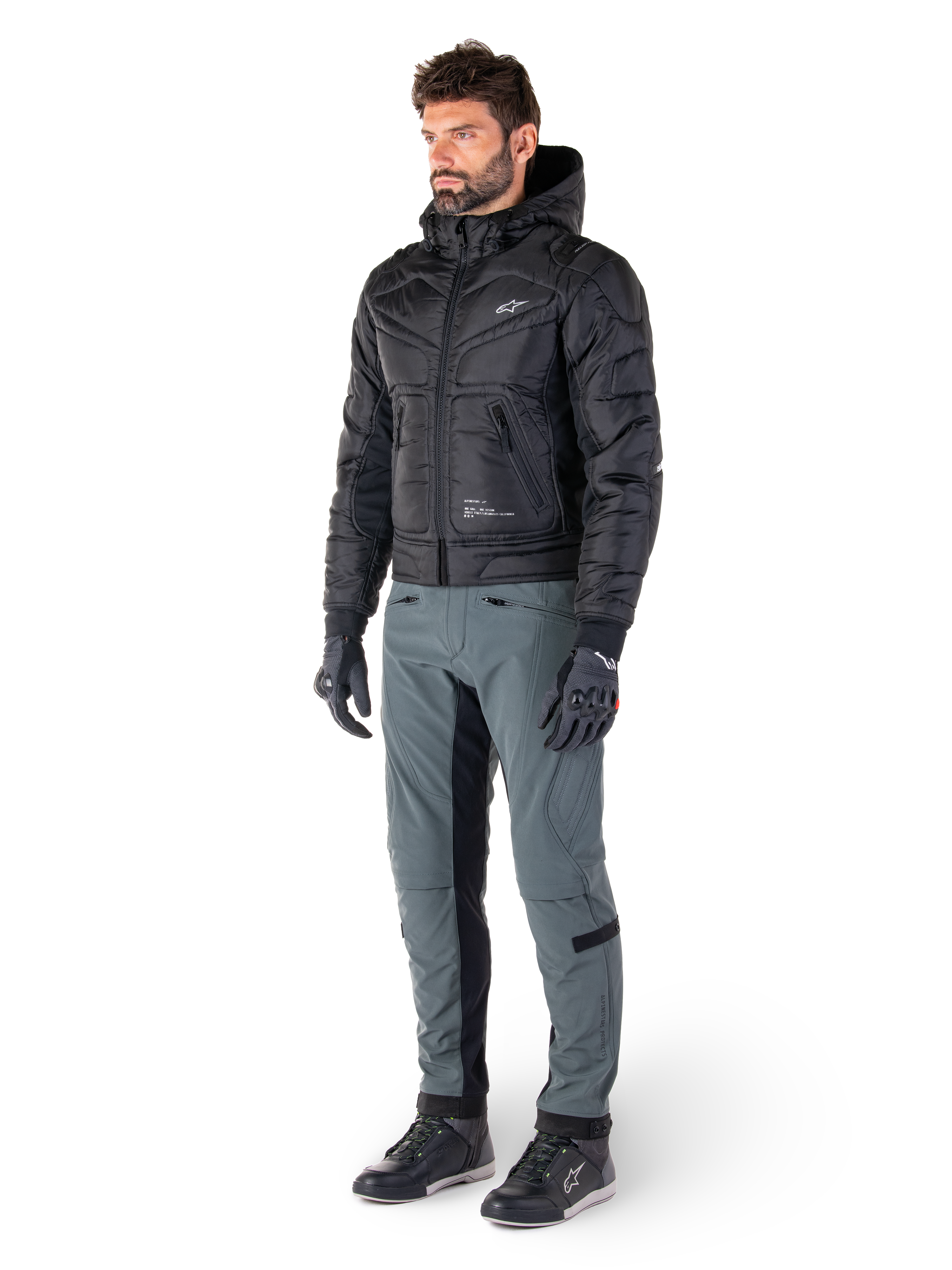 Alpinestars Mohobbs Waterproof Jacket, Black, quilted urban motorcycle bomber jacket with hood, worn by a model with grey riding pants and black gloves, featuring a white chest logo, contemporary streetwear-inspired protective gear
