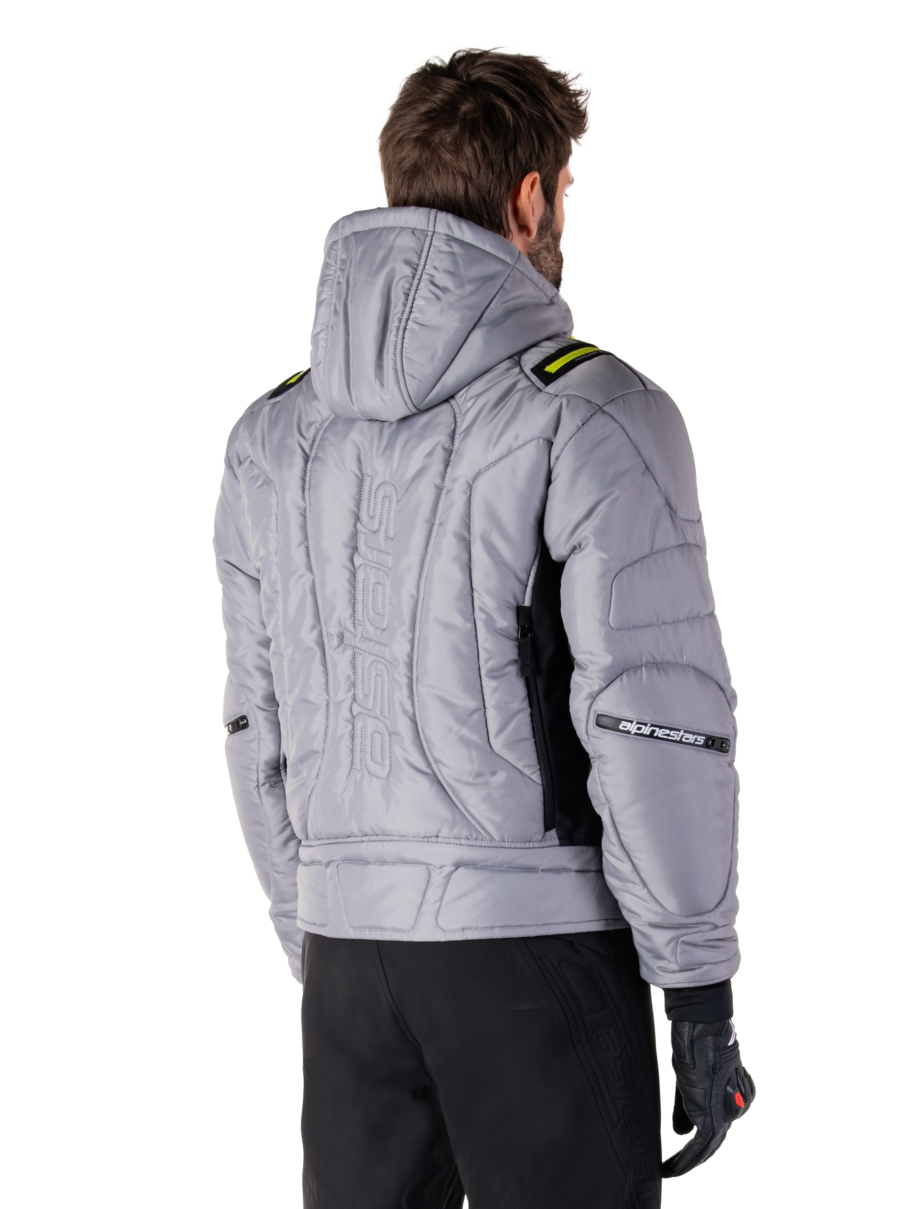 Alpinestars Mohobbs Waterproof Jacket in Lunar Gray and Lime Punch, rear view on a model, quilted padded bomber design with vertical embossed astars branding on the back, lime green shoulder accents, hooded, worn with black motorcycle pants and gloves.