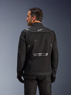 Rückansicht eines Fahrers in der Alpinestars Cusco Drystar® Jacke in Schwarz, eine Textil-Adventure-Tourenjacke mit großer Rückentasche und reflektierendem Branding, kombiniert mit passender schwarzer Hose und Handschuhen