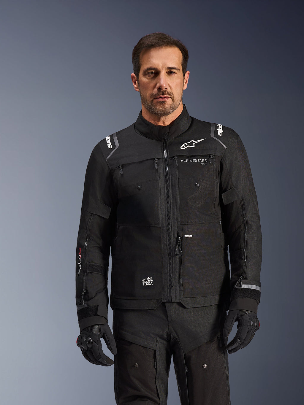Alpinestars Cusco Drystar® Jacke, schwarze Motorradjacke, getragen von einem Model mit passenden schwarzen Handschuhen und Hosen, technische Textilkonstruktion mit weißen Alpinestars-Logos, konzipiert für Road Adventure Touring