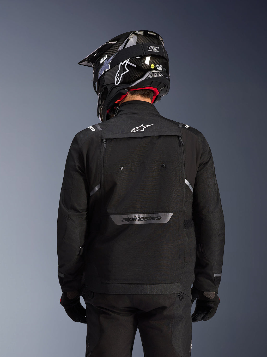 Alpinestars Cusco Drystar® Jacke, Schwarz, Rückansicht eines Fahrers mit schwarzem Helm und Handschuhen, große Belüftungspanäle, weißes Logo am Nacken und reflektierendes Branding am unteren Rücken, Adventure-Touring-Ausrüstung