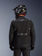 Alpinestars Cusco Drystar® Jacke, Schwarz, Rückansicht eines Fahrers mit schwarzem Helm und Handschuhen, große Belüftungspanäle, weißes Logo am Nacken und reflektierendes Branding am unteren Rücken, Adventure-Touring-Ausrüstung