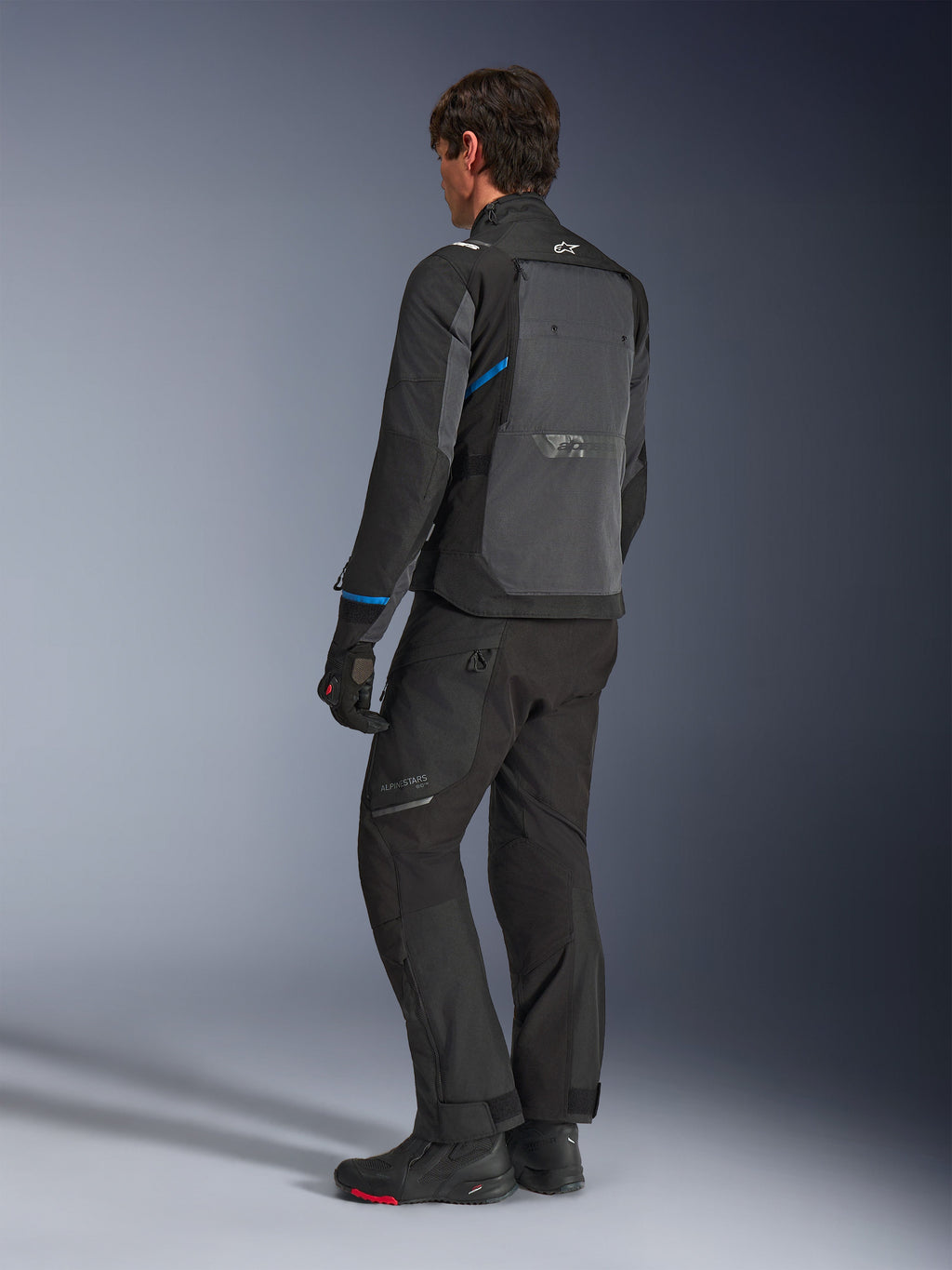 Alpinestars Cusco Drystar® Jacke, Schwarz und Dunkelgrau, Dreiviertel-Rückansicht mit großem Belüftungspanel am Rücken und blauen Akzenten an den Ärmeln, getragen mit schwarzer Motorradhose und Stiefeln für ein komplettes Touring-Outfit.